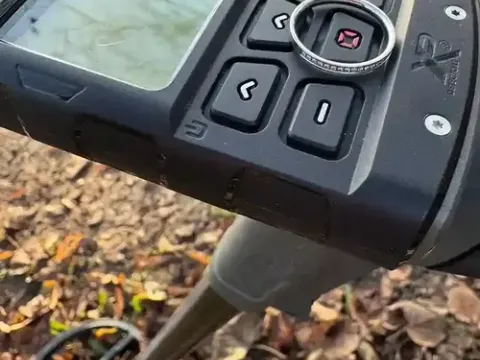 Wiedergefundener Ring auf der Spule des Metalldetektors im Laub
